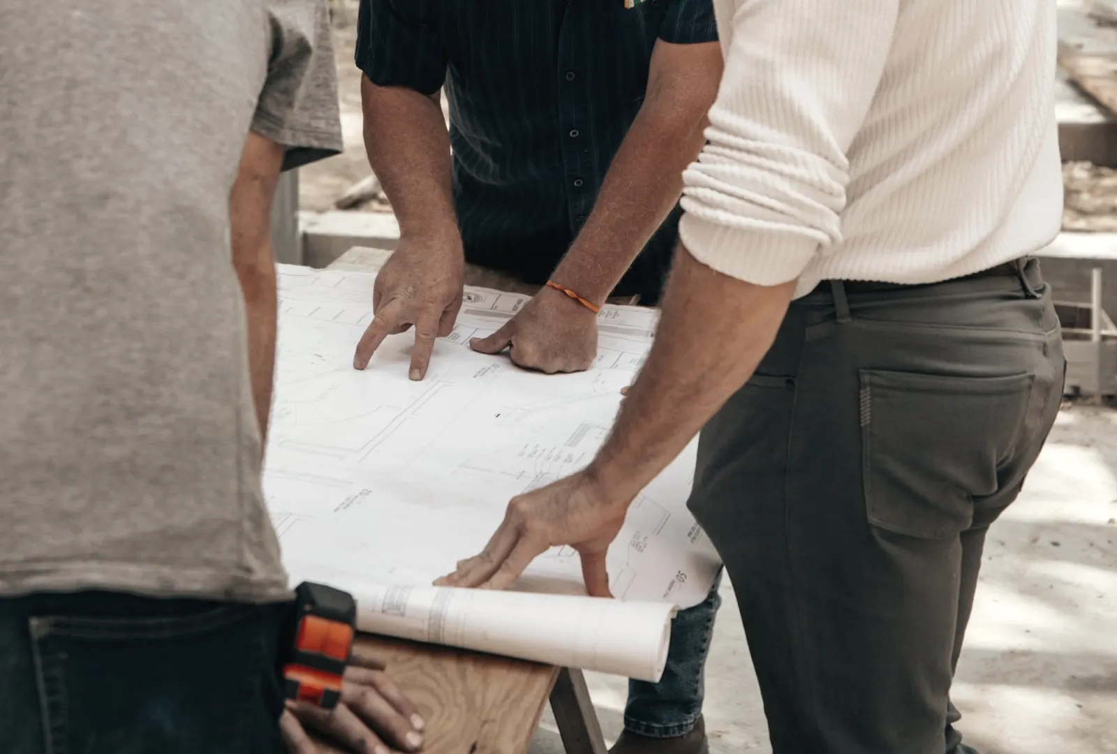 Contractors’ hands pointing to details on a building plan at a job site