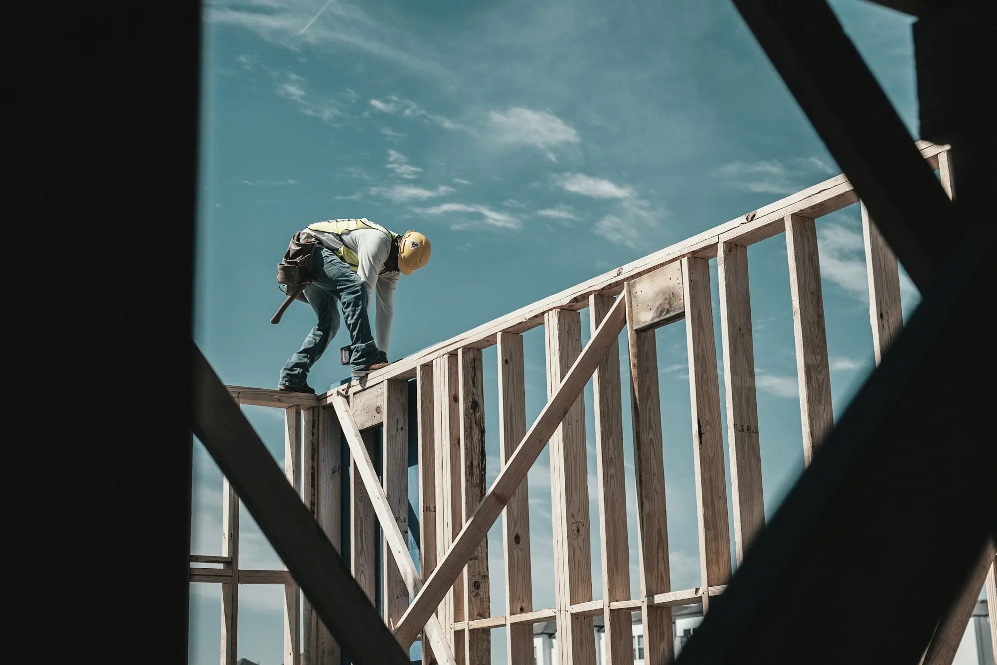 A construction worker in a hard hat working on a timber wall frame